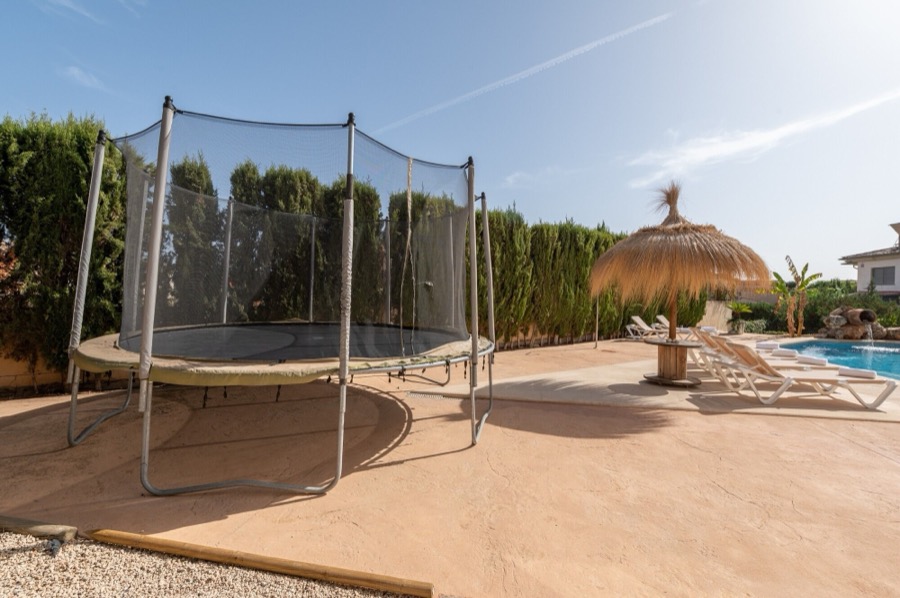 Cama elástica con red de seguridad junto a la piscina